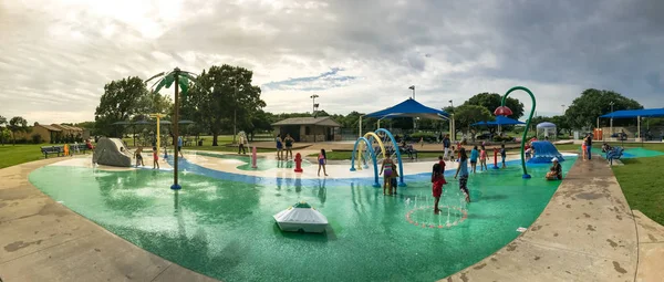 Panoráma multikulturális gyerekek és a szülő játszik a splash parkban nyáron viharos időjárás — Stock Fotó