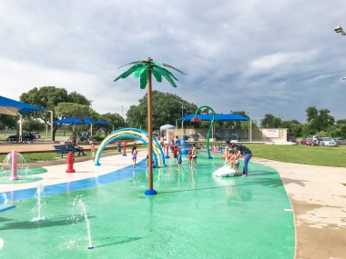 Çok kültürlü çocuklar ve ebeveyn yaz fırtınalı hava altında splash parkta oynuyor