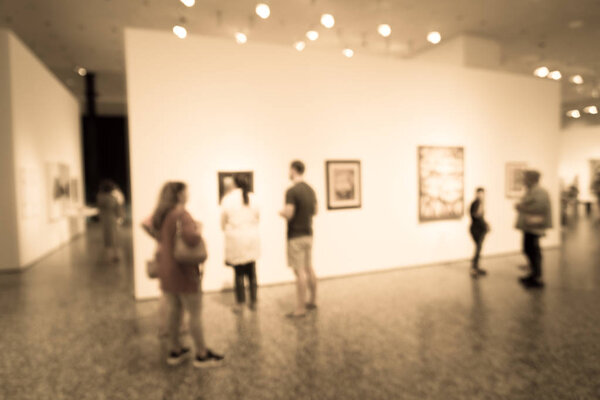Filtered image blurry background people looking at fine art display at museum in USA