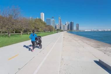 Chicago şehir merkezine doğru göl kenarında yolda bebek arabası ile çalışan Asyalı kadının geri görünümü