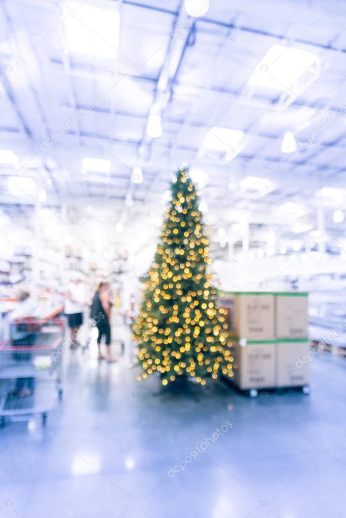 Blurry background customer shopping for giant artificial Christmas tree at wholesale store in Texas
