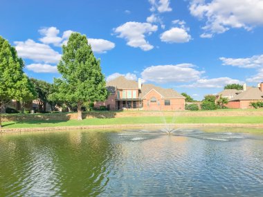 Suburban lakefront houses with water fountain and green grass lawn near Dallas clipart