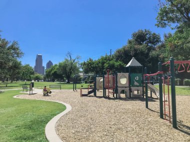 Dallas, Teksas, ABD 'de arka planda gökdelenleri olan büyük ağaçlarla çevrili boş çocuk parkı