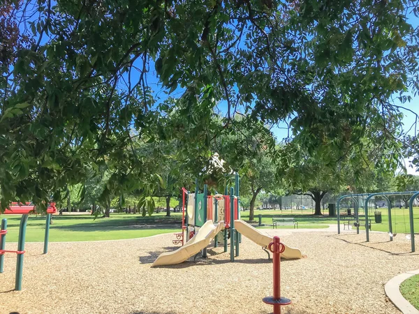 Skuggig från stora träd och färgglada urban lekplats i offentlig park i centrala Dallas, Texas, USA — Stockfoto