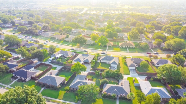 Urban sprawl near Dallas, Texas, USA with row of single family houses and large fenced backyard. Aerial view residential neighborhood subdivision surrounded by mature trees in early summer morning