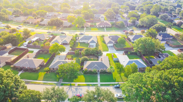 Drone view clean and empty neighborhood street with row of single family houses near Dallas, Texas, America. Suburban home with bungalow homes and large fenced backyard in early summer morning