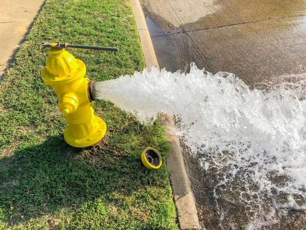 Vista lateral aberta hidrante de fogo amarelo jorrando água através de uma rua residencial perto de Dallas, Texas, EUA — Fotografia de Stock