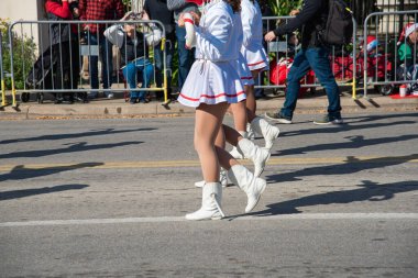 Ağır sırt çantalı bir adam, Dallas 'taki şenlikli Noel gösterilerinde beyaz etekli, botlu bir grup gösteri sanatçısının yanında duruyor. Farklı kitleleri ve sokakları ayıran çelik barikatlar. ABD