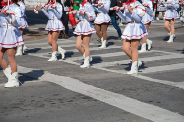 Beyaz etekli ve kırmızı aksanlı üniformalı oyuncular, diğer kırmızı kostümlü ve günlük kıyafetli katılımcılarla birlikte yürüyorlar. Bayram kıyafetleri mevsimsel neşeyi ve halk kutlamasını yansıtır. ABD