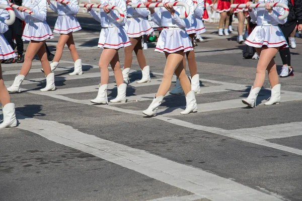 Beyaz etekli ve kırmızı aksanlı üniformalı oyuncular, diğer kırmızı kostümlü ve günlük kıyafetli katılımcılarla birlikte yürüyorlar. Bayram kıyafetleri mevsimsel neşeyi ve halk kutlamasını yansıtır. ABD