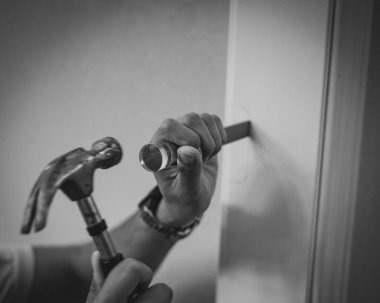 Yan görünüş el oymacılığı Asyalı tamircinin çekiçle beyaz kapı çerçevesine yatar. Dijital akıllı seğirme görünüyor. Rehberli işaret, dikdörtgen arayı oyuyor. DIY görevi hassasiyeti gösterir. ABD