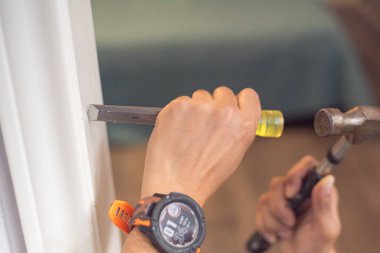 Panorama Manzarası, Asyalı tamirci tarafından çekiçle beyaz kapı çerçevesine yapılan keski menteşesi teneffüsünün ilk süreci. Akıllı seğirme görünür. Rehberli işaret, dikdörtgen arayı oyuyor. Görev hassasiyeti. ABD