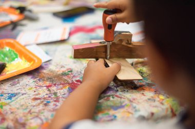 Renkli boya sıçramış atölye masası ve yakın plan Asyalı erkek elleri tahta uçak, yakınlardaki yapıştırıcı, küçük parçalar, turuncu tepsiler, çocuk atölyesinde basılı talimatlar kullanarak. ABD