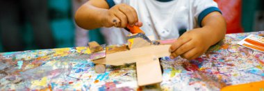 Panorama manzaralı renkli atölye masası ve yakın plan Asyalı erkek elleri tahta uçak, yakın tutkal, küçük parçalar, turuncu tepsiler, yazılı talimatlar kullanarak. ABD