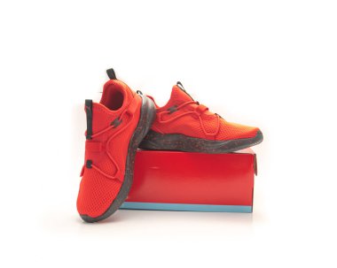 Kırmızı spor ayakkabılar, siyah benekli lastik tabanlar ve beyaz arka planda izole edilmiş ağ yükselticilerle uyumlu ayakkabı kutusunda sergileniyor. Düz ve eğik tasarım vitrinler ambalaj, fit, perakende sunumu. ABD