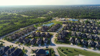 Curved rows of homes in Lantana, Texas, surround central pond, with dense forest stretching to the horizon. Captures suburban planning, natural land integration border by FM 407 and Justin Road. USA
