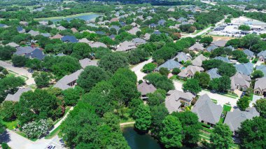 Commercial zone business buildings in background from upscale residential neighborhood with scenic pond and water fountain in Colleyville, Texas, large mansion house, swimming pools, grassy yard. USA