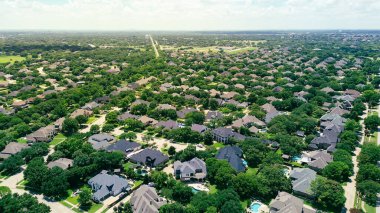 Downtown Fort Worth Texas in distant background from Colleyville, residential street along row of upscale two-story suburban homes nestled in mature trees, swimming pools, dense greenery backyard. USA