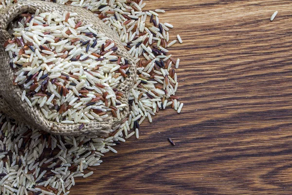 Πολύχρωμο ρύζι σε μια σακούλα σε ένα ξύλινο υπόβαθρο — Φωτογραφία Αρχείου
