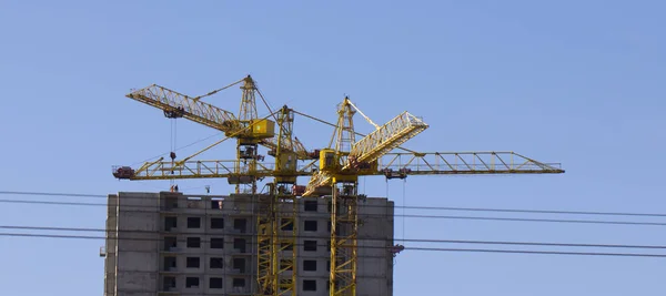 Gru a torre contro il cielo blu, il processo di costruzione di un edificio a più piani — Foto Stock