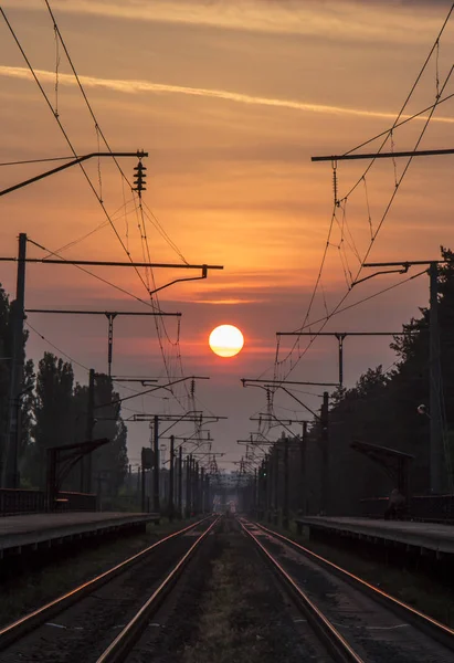 Gün batımında, bir platform ozhidayuschimi yolcular ile Demiryolu demiryolu