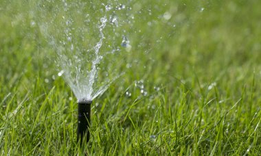 Otomatik fıskiye sistemi yeşil çimlerin arka planında çimleri suluyor