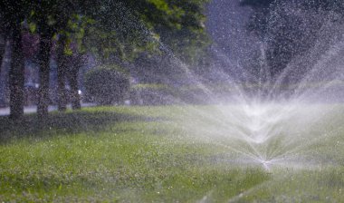 Otomatik fıskiye sistemi yeşil çimlerin arka planında çimleri suluyor