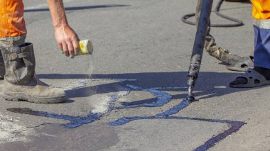 İşçiler yol onarım, daha fazla yol yüzeyi imha önlemek için bitüm ile küçük çatlaklar dökün. Yakın çekim