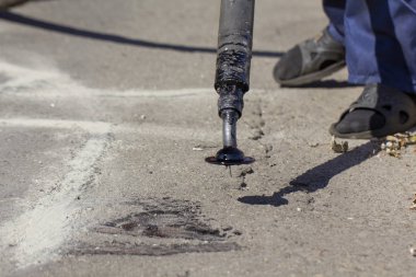 İşçiler yol onarım, daha fazla yol yüzeyi imha önlemek için bitüm ile küçük çatlaklar dökün. Yakın çekim