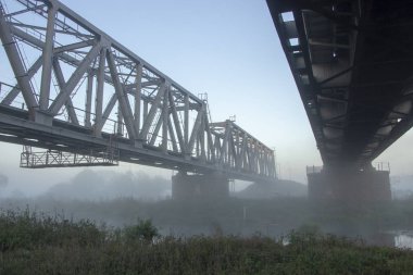 Sabah sisinde bir demiryolu köprüsü ya da güneş ışınlarının arka planda parladığı bir duman..