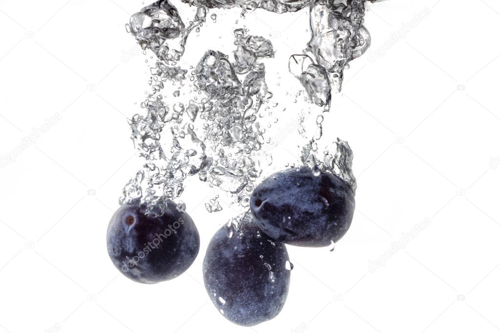 Plums falling into water, isolated on a white background, close up