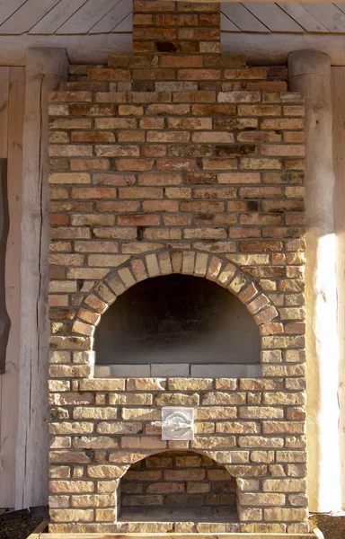 Brick fireplace outside the house, near a wooden wall, on a clear sunny day
