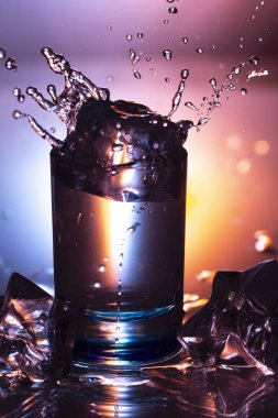 Bir bardak su ve su sıçramalarına koyu renkli arka plan üzerinde dışarı knocking bir buz küpü yakın çekim