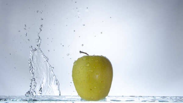 Green apple on a light background and splashing water close up
