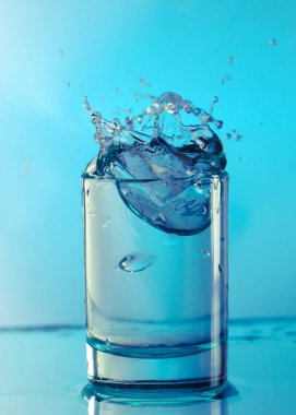 Saf içme su sıçramalarına açık yeşil arka planı üzerinde yuvarlak bir cam ile yakın çekim