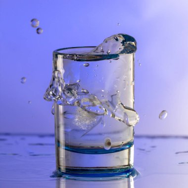 Saf içme su sıçramalarına bir ışık mor arka plan üzerinde yuvarlak bir cam ile yakın çekim