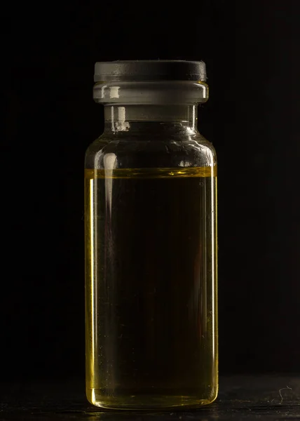 small medical Bottle, with yellow inside, on a black background, close-up, selective focus