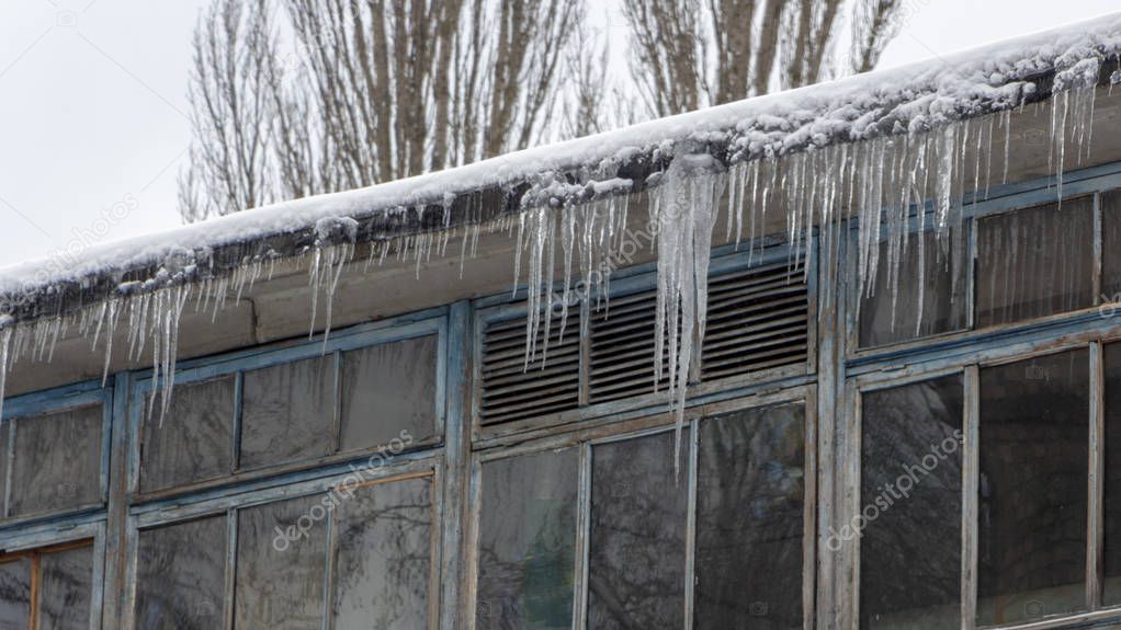 Icicles on the drainpipe and ditch. Incorrect installation of the drainage system, on which large icicles appear that pose a threat to the health and lives of people