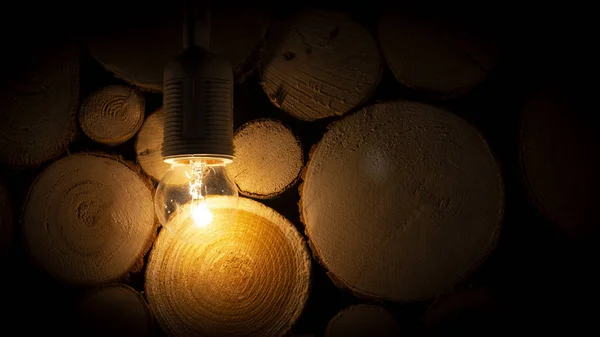 Dim light bulb on the background of a wooden log wall