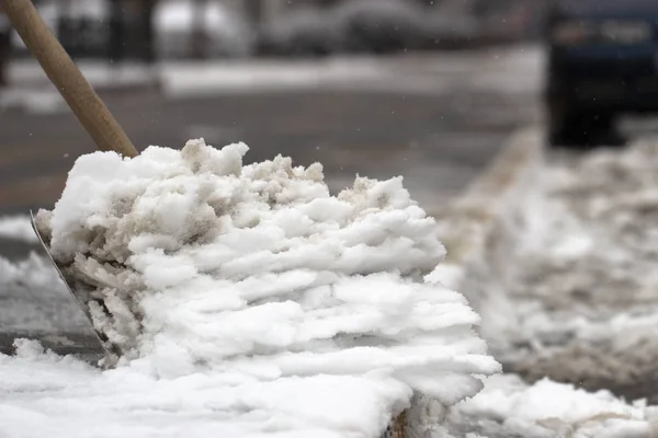 Man with snow shovel cleans sidewalks in winter street.
