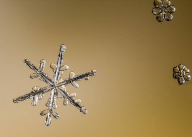 Beautiful snow flake on light orange background close-up
