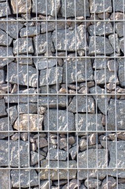 Gabion, a stone wall with a metal grid of gray granite texture