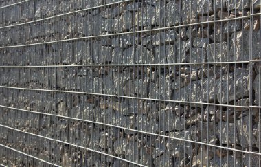 Gabion, a stone wall with a metal grid of gray granite texture