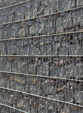 Gabion, a stone wall with a metal grid of gray granite texture