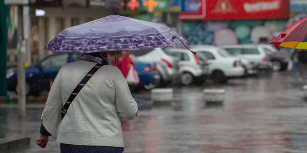 La gente si nasconde dalla pioggia sotto gli ombrelloni in una giornata piovosa sulla strada della città concetto di cattivo tempo — Foto Stock