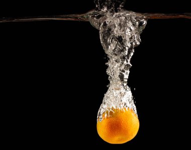Mandalina siyah bir arka plan üzerinde sprey oluşturarak suya düşüyor