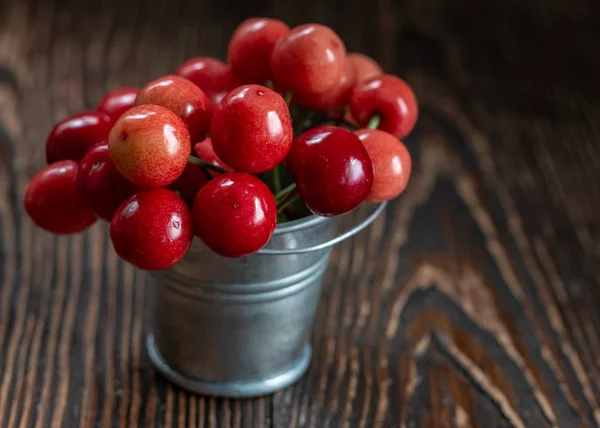 Fresh red Cherries in small metal bucket on old wooden background rural style