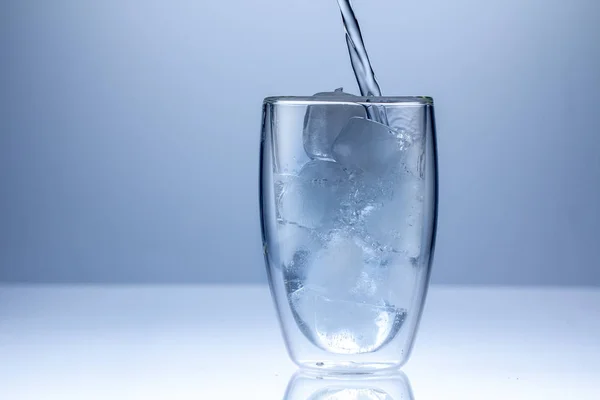 Despejando água em vidro no fundo azul fechar — Fotografia de Stock