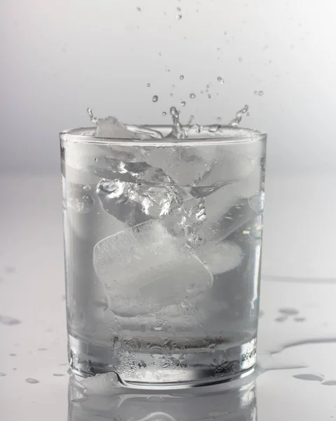 Borrife a água em um copo em um contexto cinza — Fotografia de Stock