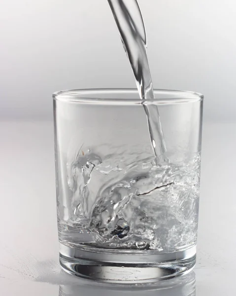 Stříkání vody ve skle na šedém pozadí — Stock fotografie